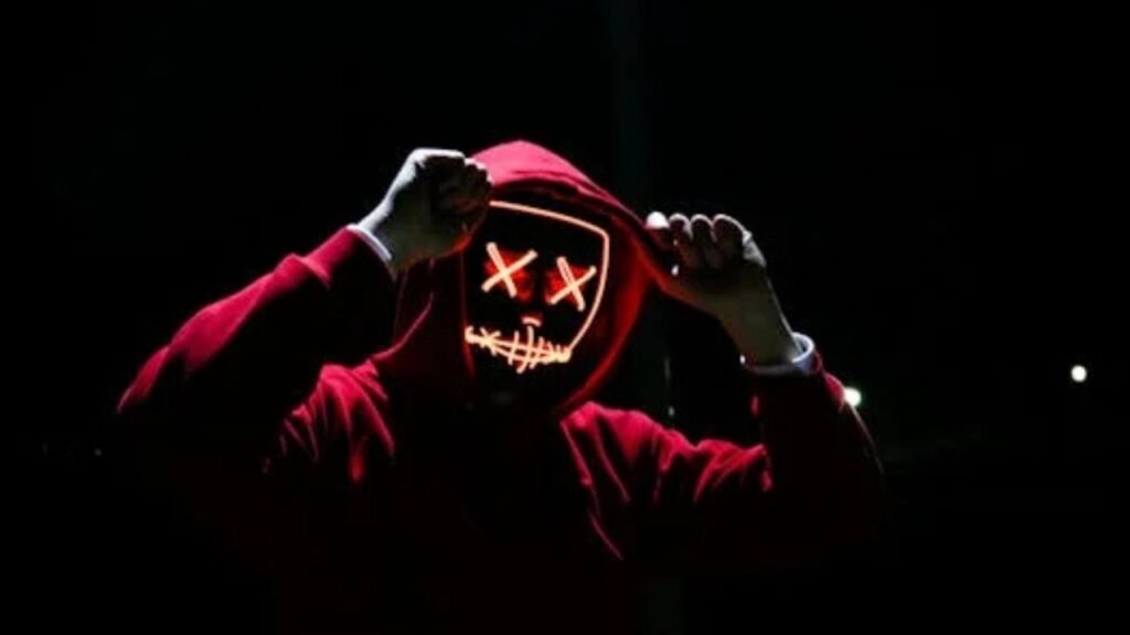 A spooky illuminated mask figure with a red hoodie in a dark setting, perfect for Halloween themes