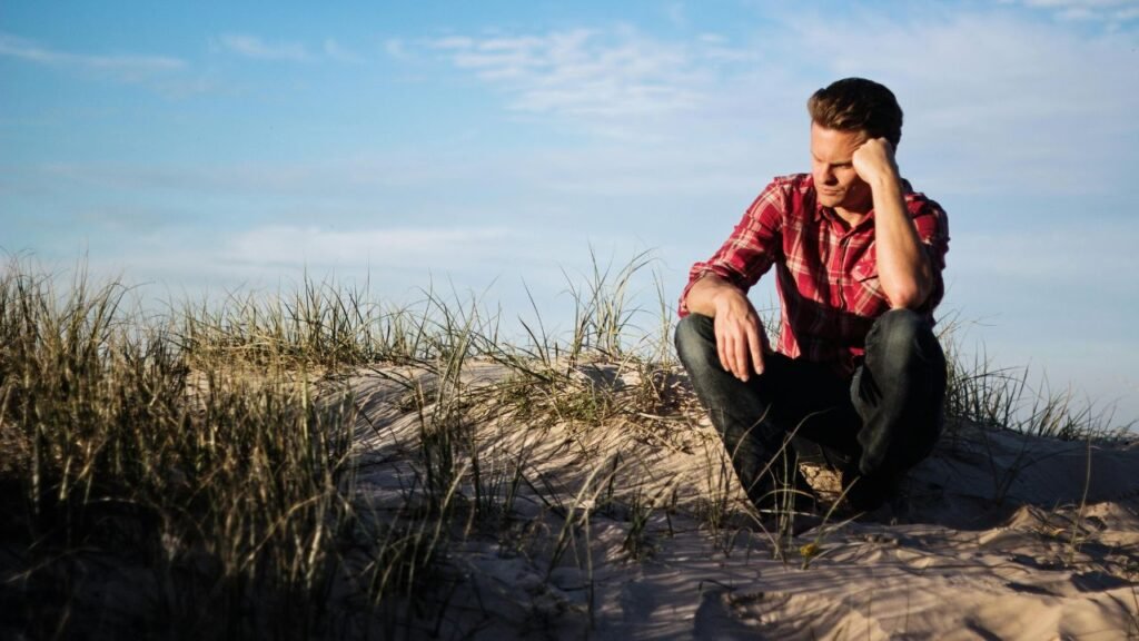 Man sitting on sand dunes looking thoughtful representing an identity shift during personal growth and self reflection