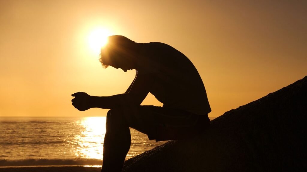 Silhouette of a man sitting by the ocean at sunset, thinking about how to find meaning in life and personal purpose