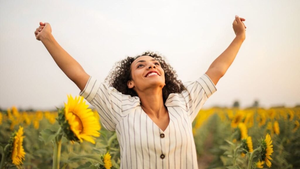 Smiling woman with raised arms among sunflowers