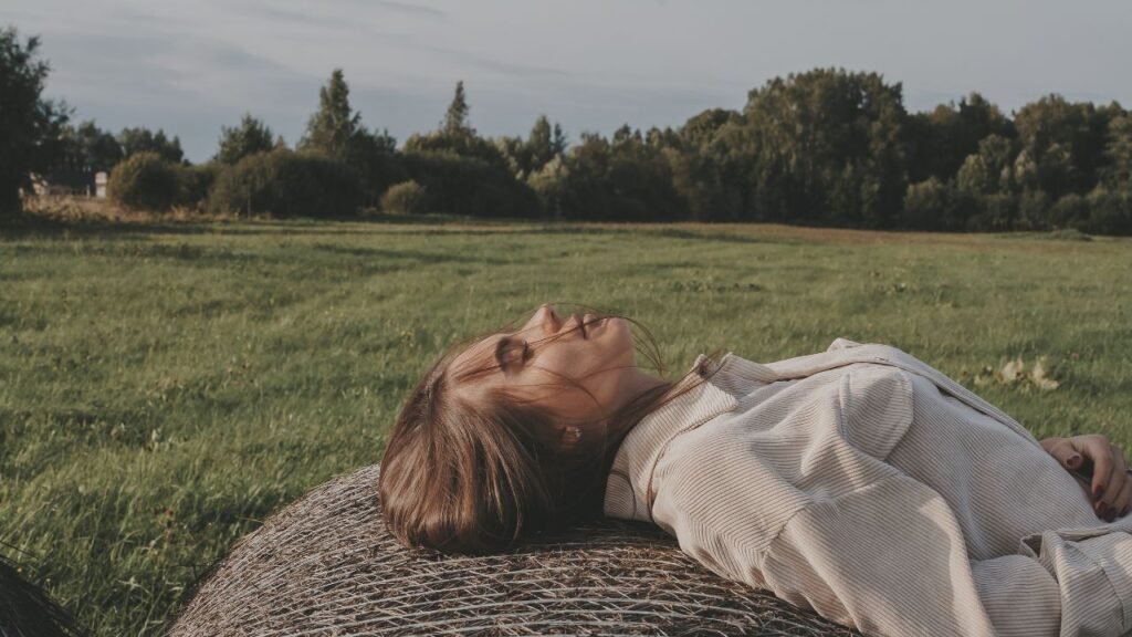 Woman lying on a hay bale in an open field, resting and looking upward