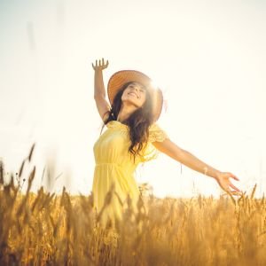 Home 9 Woman standing in a sunlit field with arms raised, symbolizing personal growth and freedom