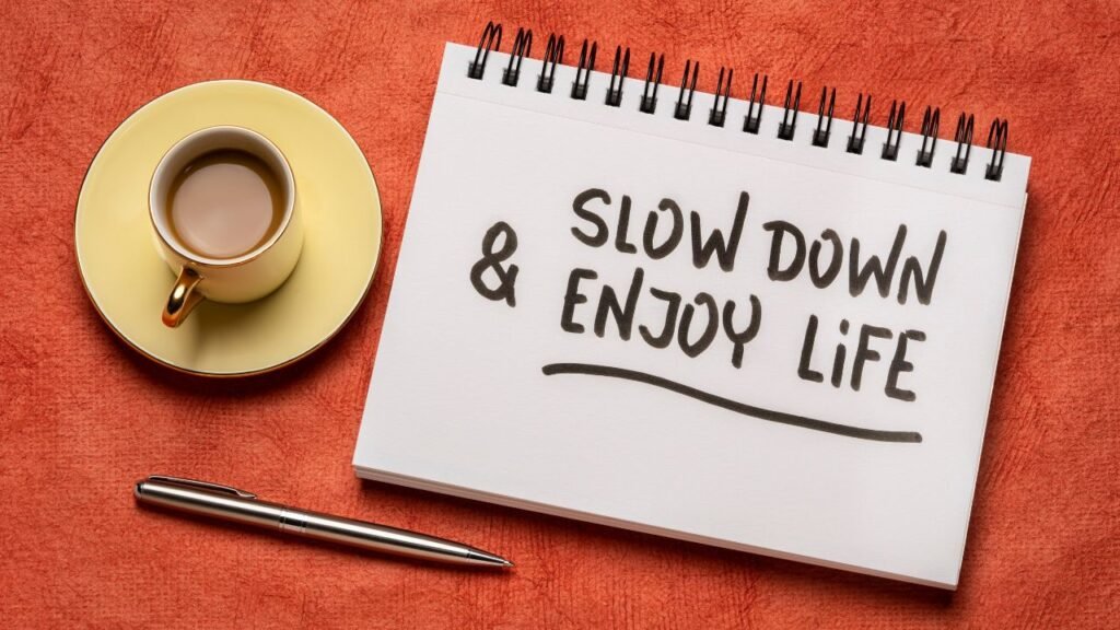 Notebook with “slow down and enjoy life” beside coffee and pen, representing the benefits of slowing down