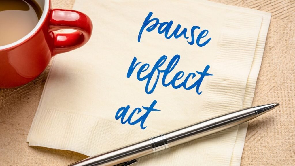 Notebook with words “pause reflect act” beside a coffee cup and pen