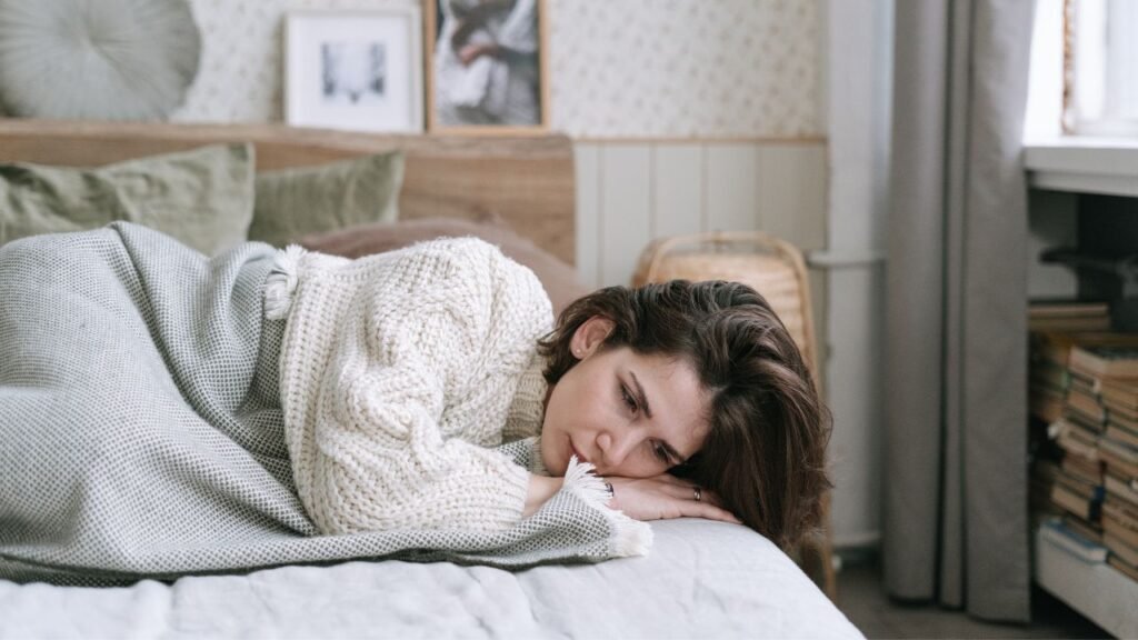 Woman lying on bed looking tired and emotionally drained in a cozy bedroom, showing why slowing down is a necessary part of personal growth