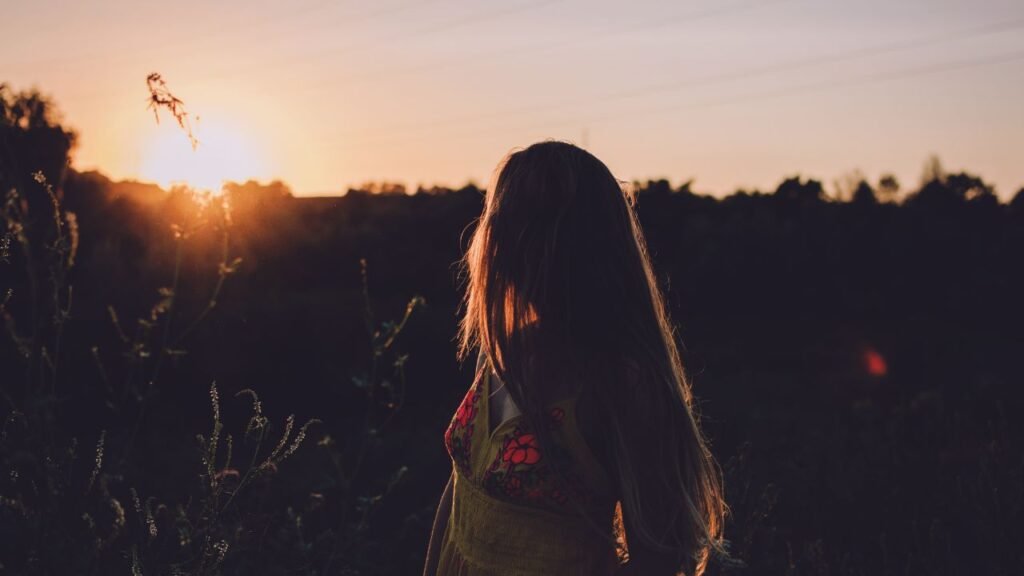 Woman standing in a field at sunset reflecting quietly, showing the benefits of slowing down