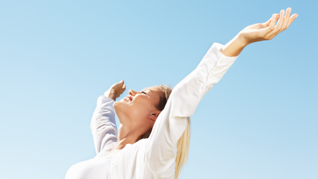 How to Let Go of Your Old Self Without Fear 4 Smiling woman with open arms under clear skies, showing the peace that comes from learning how to let go of your old self