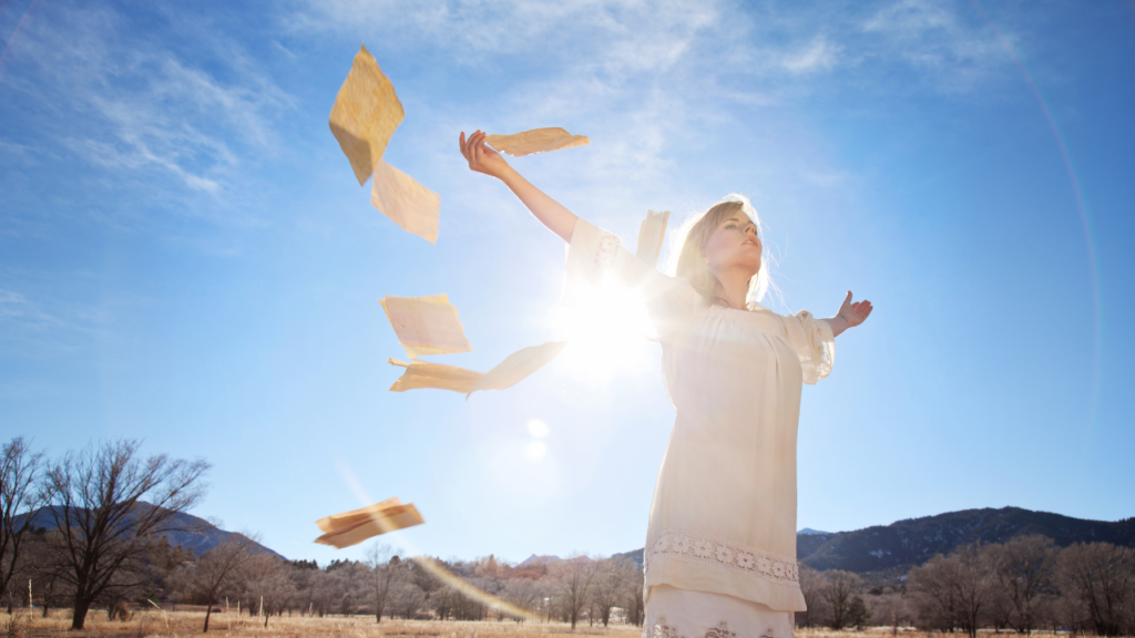 How to Let Go of Your Old Self Without Fear 3 Woman releasing papers into the air under the bright sky, symbolizing how to let go of your old self and embrace freedom