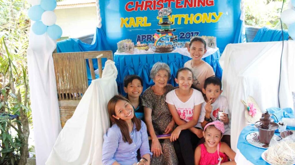 Ninety-Three Years of Love: What Lola Inay Taught Me About a Life Well Lived 3 Family gathered around a christening celebration with blue decorations and a dessert table